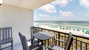 Een balkon met uitzicht op het strand, voorzien van een tafel, stoelen en een hekwerk.