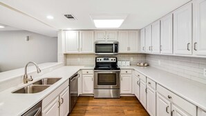 Een moderne keuken met witte kasten, roestvrijstalen apparatuur en een houten vloer.