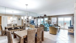 A spacious living area with a wooden dining table, wicker chairs, a sofa, and a balcony with a view of the sea. - Updated, beachfront condo with beach setup - quick drive to entertainment (Fort Walton Beach)