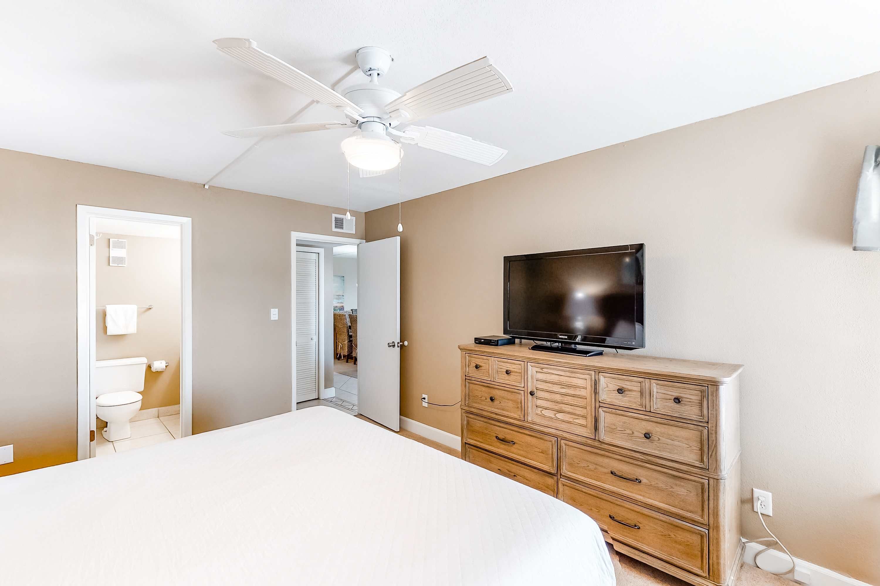 A bedroom with a bed, a dresser, a television, and a ceiling fan.