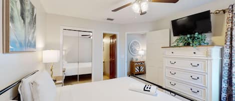 A hotel room with a bed, a ceiling fan, a TV, a dresser, and a plant.