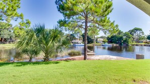 A serene lakeside view with a hammock, a hammock chair, and a small dock with a boat. - Condo close to the beach with pools, dock & tennis - snowbird-friendly (Panama City Beach)