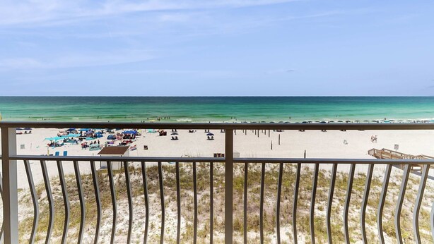 Blick auf einen Strand vom Balkon mit Geländer, feiner Sand und klarer, blauer Himmel.
