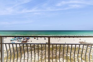 Blick auf einen Strand vom Balkon mit Geländer, feiner Sand und klarer, blauer Himmel.