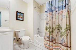 Un baño con inodoro, bañera y cortina de ducha con motivos playeros.