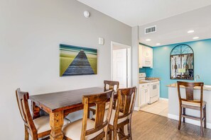 Un comedor con una mesa y sillas de madera, una cocina con armarios blancos y una pared azul decorativa.