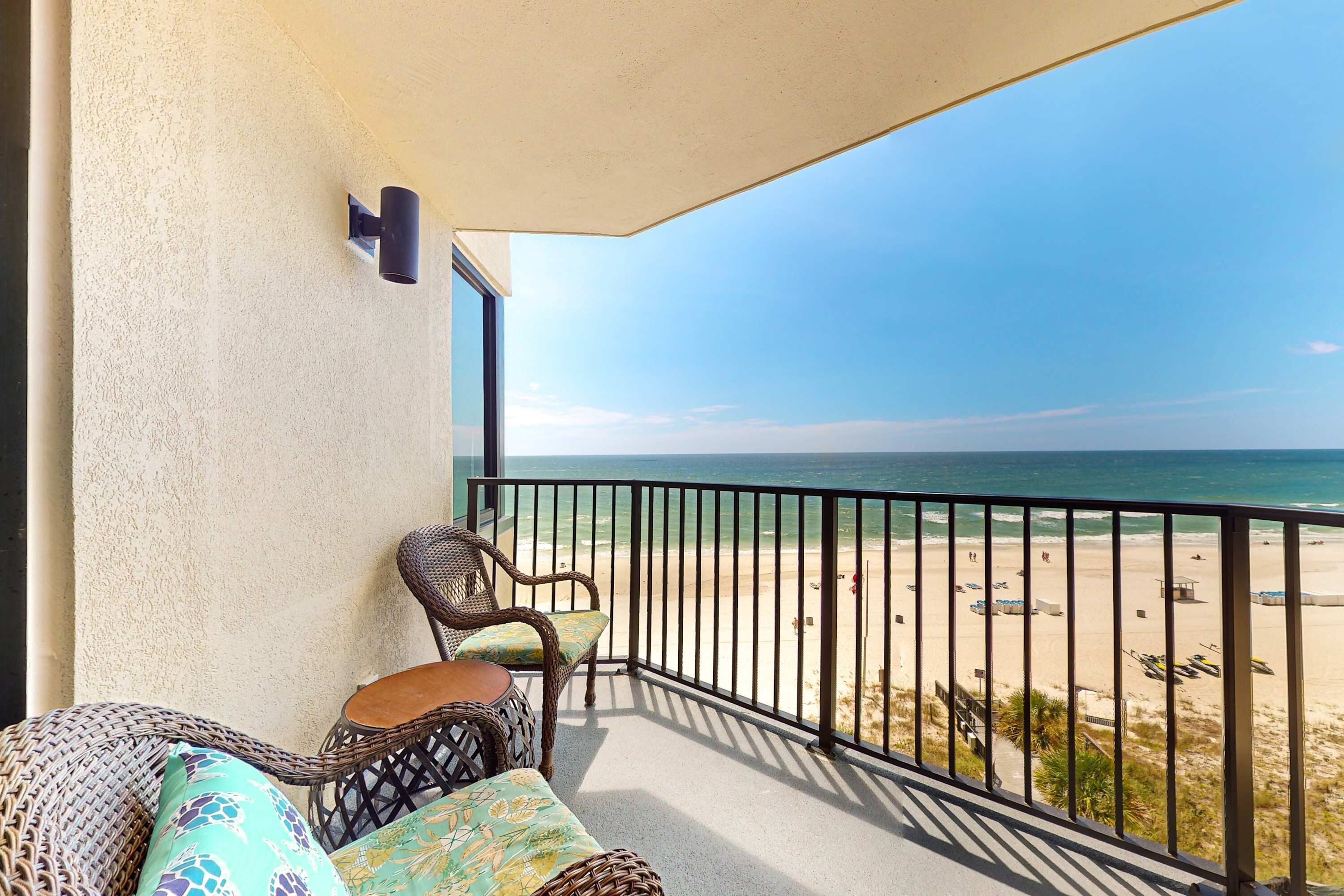A balcony with a view of the beach, wicker furniture, and a small table.