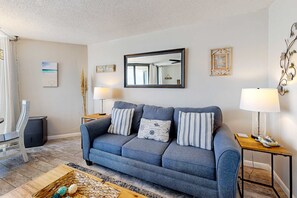 A living room with a blue sofa, two side tables with lamps, a large mirror, and decorative wall art. - Gulf-view condo with pools, beach access, gym, grills, & updated interior (Panama City Beach)
