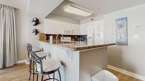 Een moderne keuken met witte kasten, een magnetron en een klein eiland met barkrukken.