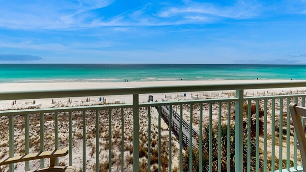 Uitzicht op een strand vanaf een balkon met een balustrade, een zandstrand en de oceaan.