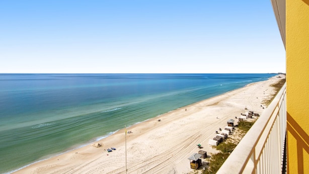 Uitzicht op het strand vanaf een balkon, met een heldere lucht, zandstrand en een rij strandhutten.