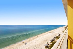 A beach view from a balcony with a clear sky, sandy beach, and a row of beach huts. - Stylish Gulf-front condo steps from the beach with resort pool, hot tub & gym (Panama City Beach)