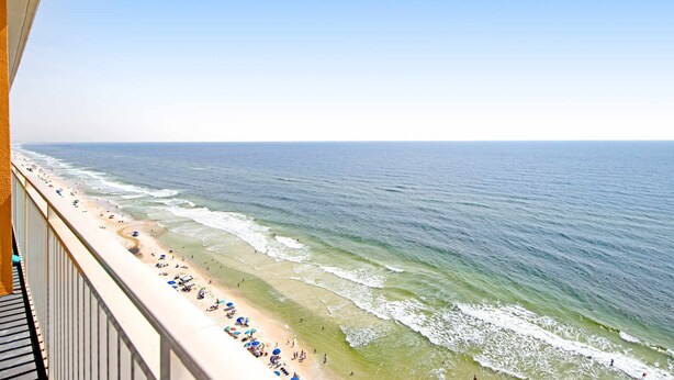 Une vue sur la plage depuis un balcon doté d’une balustrade, avec les vagues de l’océan et des personnes sur la plage.