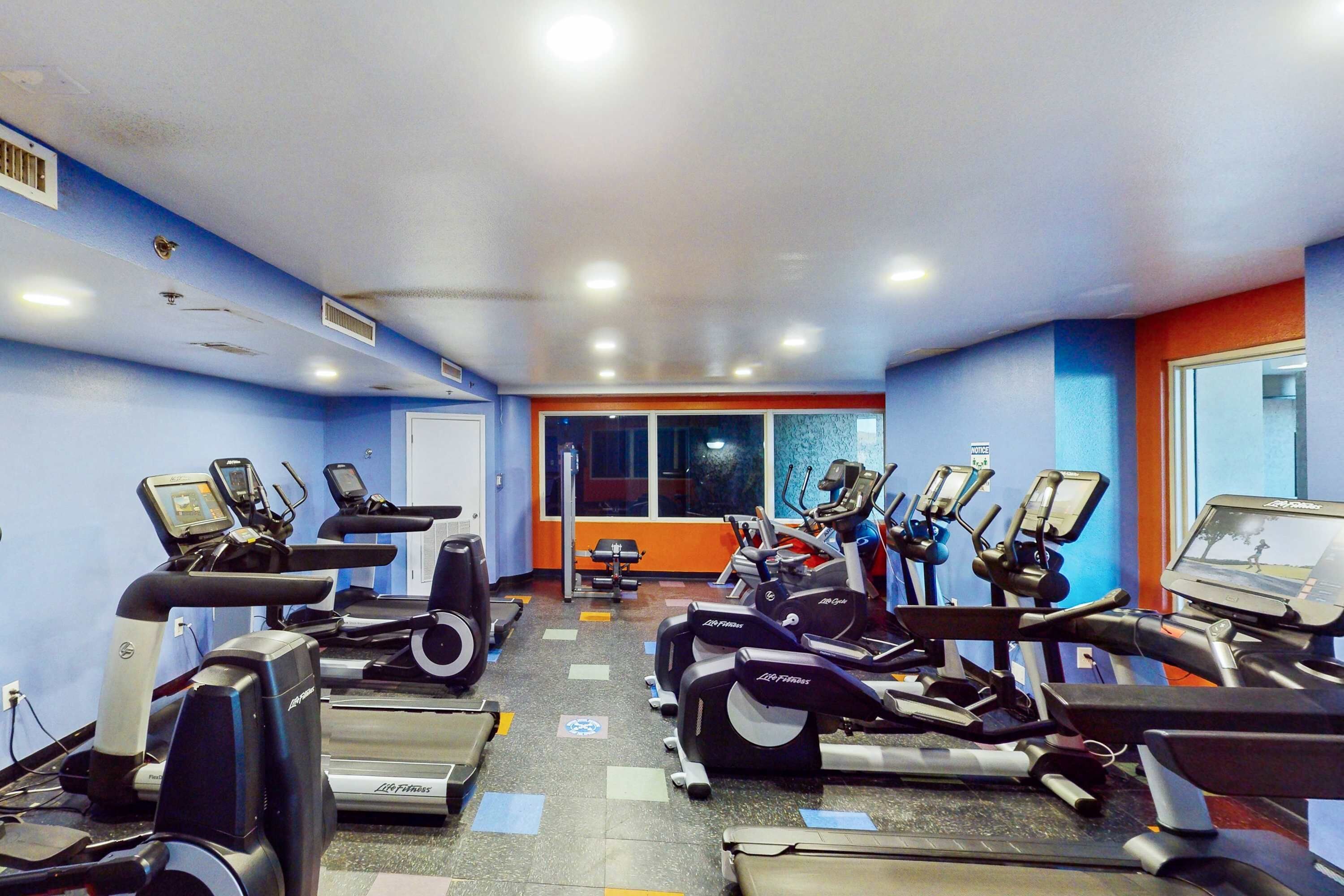 A gym with multiple treadmills and exercise bikes, a window with a view, and a door with a sign.