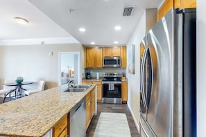 A modern kitchen with granite countertops, stainless steel appliances, wooden cabinets, and a central island. - Beachfront dream with furnished balcony, pool & gym (Panama City Beach)