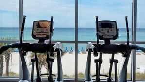 An indoor exercise area with two stationary bikes, large windows, and a view of the beach. - Fifth-floor oceanfront condo with high-speed WiFi, Gulf view, Pools & Hot tub (Panama City Beach)