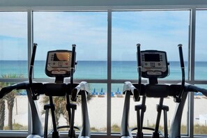 An indoor exercise area with two stationary bikes, large windows, and a view of the beach. - Fifth-floor oceanfront condo with high-speed WiFi, Gulf view, Pools & Hot tub (Panama City Beach)