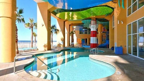 An indoor swimming pool with a view of the ocean, palm trees, and a colorful play area. - Fifth-floor oceanfront condo with high-speed WiFi, Gulf view, Pools & Hot tub (Panama City Beach)