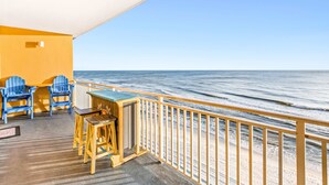A balcony with a view of the ocean, featuring a wooden table and two blue chairs. - Fifth-floor oceanfront condo with high-speed WiFi, Gulf view, Pools & Hot tub (Panama City Beach)
