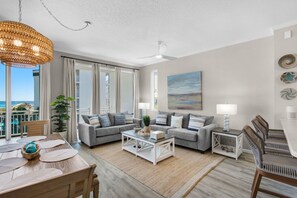 A modern living room with a sofa set, a coffee table, and a dining area with a wooden table and chairs. - Beautiful 2nd-floor condo in Seagrove Beach with beach ambience & pickleball (Santa Rosa Beach)