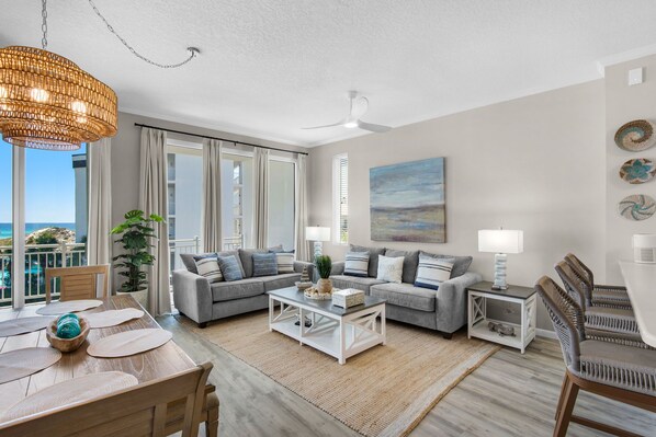 A modern living room with a sofa set, a coffee table, and a dining area with a wooden table and chairs. - Beautiful 2nd-floor condo in Seagrove Beach with beach ambience & pickleball (Santa Rosa Beach)