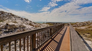 Une promenade en bois qui mène à une plage, avec un ciel dégagé.
