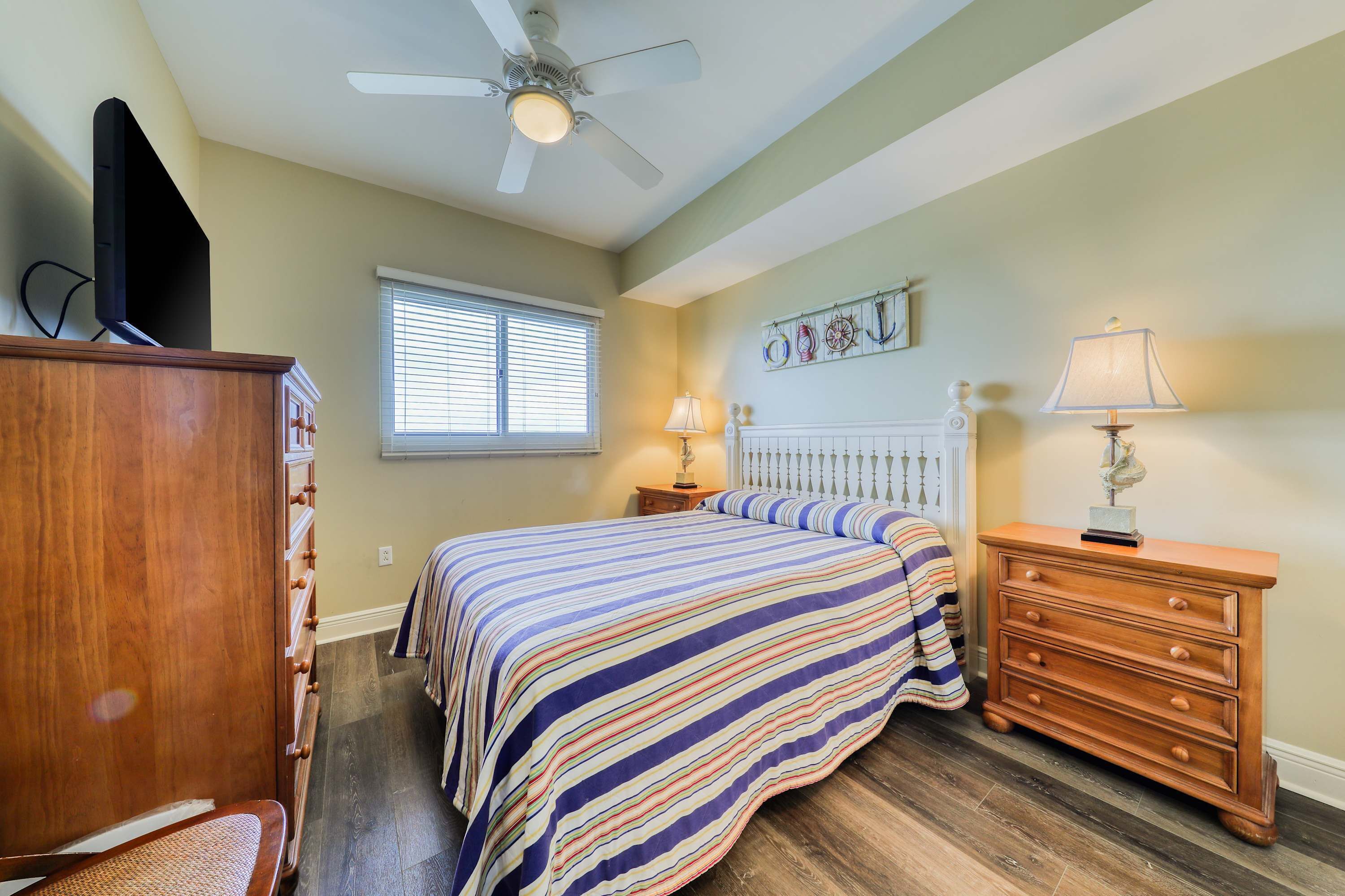 A bedroom with a bed, dresser, nightstand, and a ceiling fan.