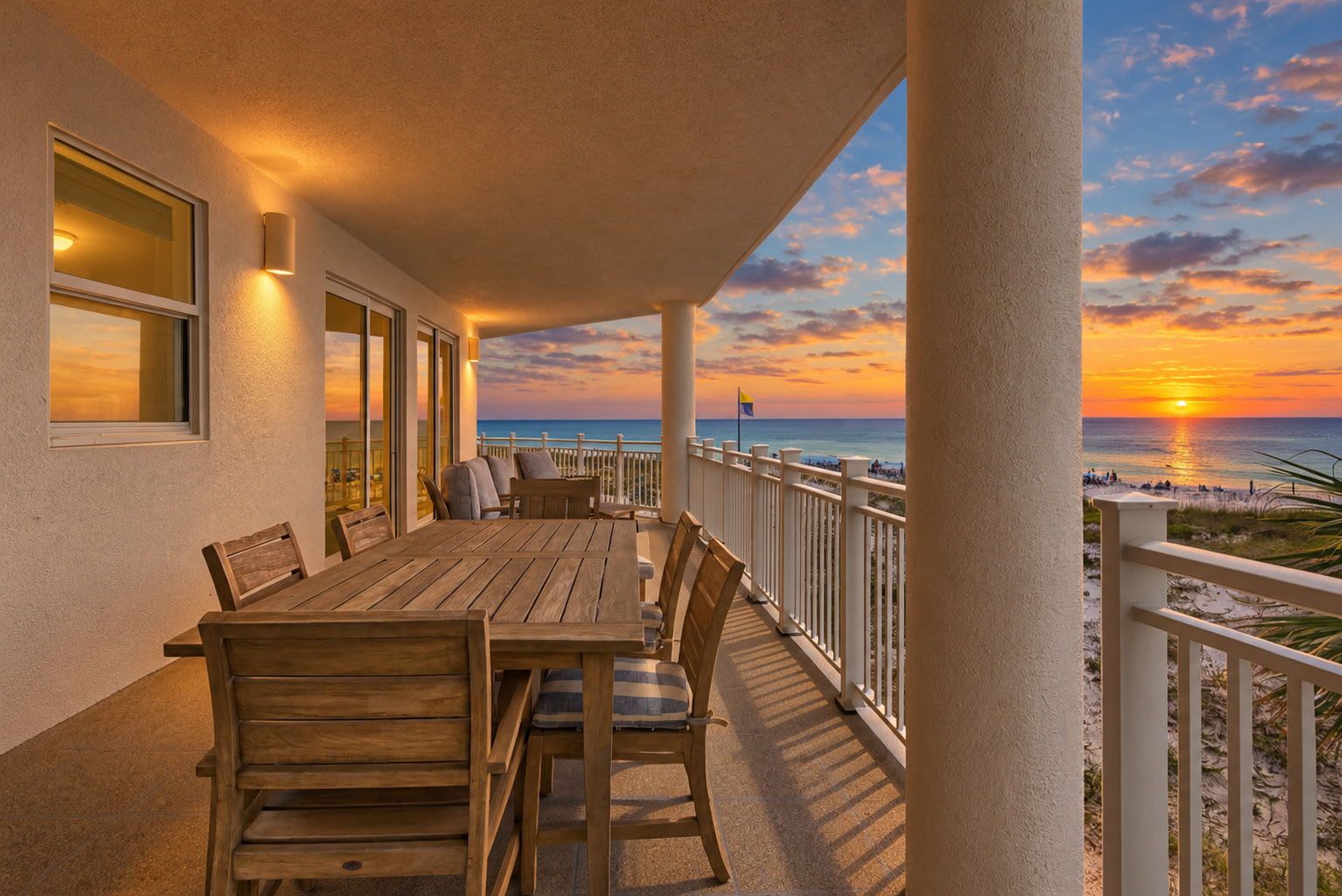A wooden table and chairs on a balcony with a view of the sunset over the ocean.