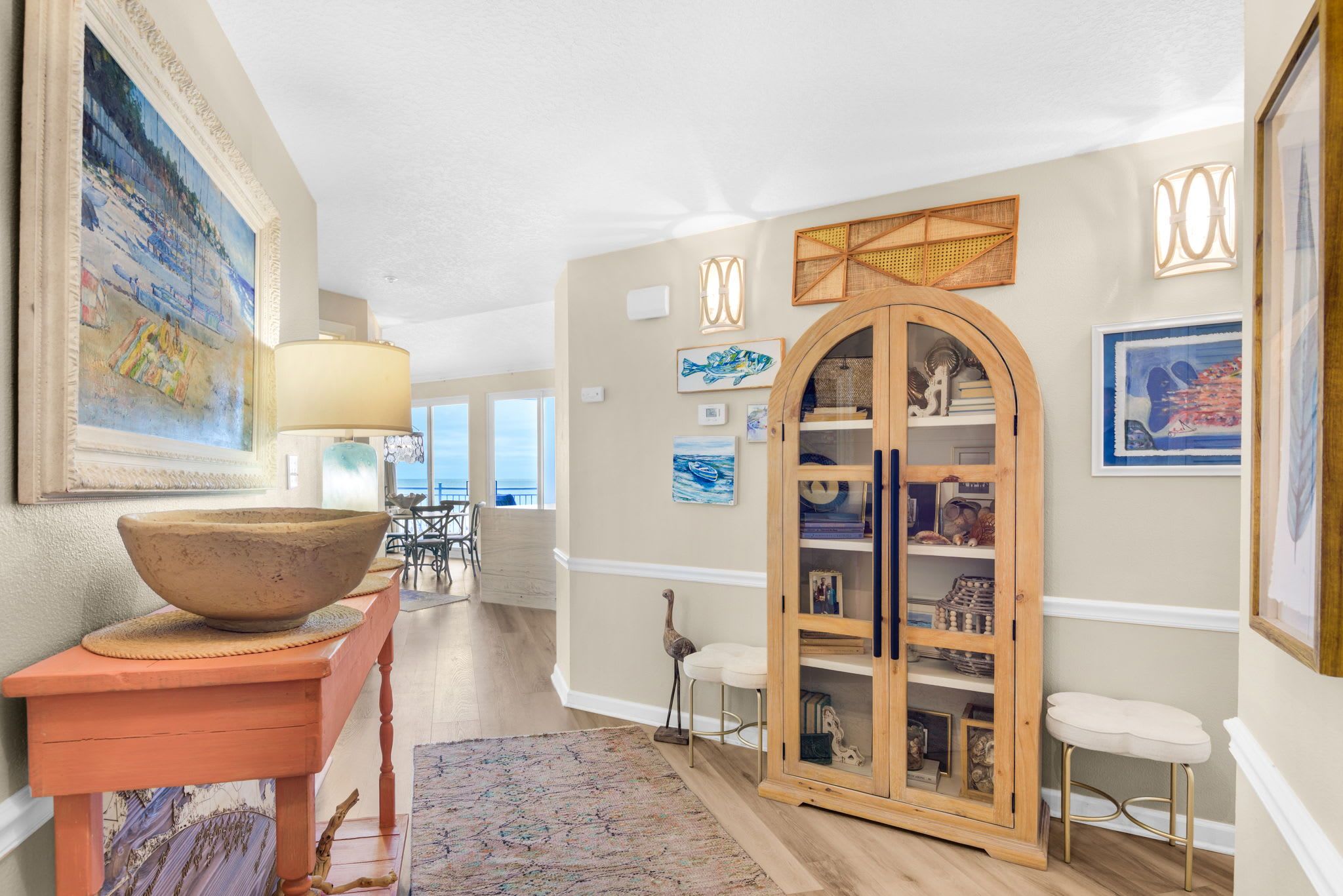 A well-lit hallway with a wooden cabinet, a table with a bowl, and artwork on the walls.