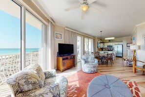 A spacious living room with a large TV, comfortable seating, a kitchen area, and a balcony with a view of the beach. - Gulf-front 3-bedroom condo with bonus bunk room & pickleball (Santa Rosa Beach)