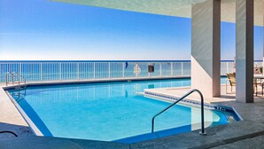 Una piscina azul cristalina con barandilla blanca, una silla de salvavidas y vistas al océano.