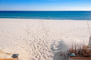 Una spiaggia sabbiosa con impronte che conducono all'acqua, una recinzione di legno e un cielo azzurro limpido.