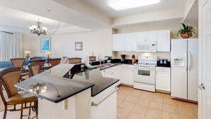 Een moderne keuken met witte kasten, een zwart aanrecht en een centraal eiland. Er is een zithoek met stoelen en een kroonluchter.