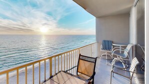 Een balkon met uitzicht op zee, een tafel, twee stoelen en een hekwerk.