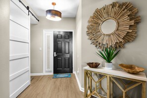 A hallway with a black door, a round mirror on the wall, a wooden console table, and a plant. - 3rd-floor condo with sauna, gym, pool, tennis & pickleball, conference room (Santa Rosa Beach)