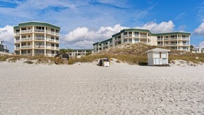 Et hotel ved stranden med flere balkoner, en redningsplatform og en sandstrand.