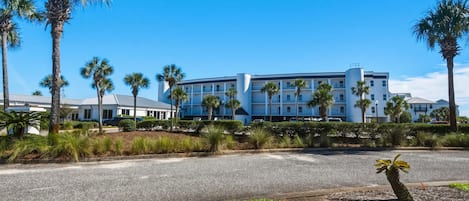Un hôtel au design moderne, caractérisé par une structure cylindrique centrale, de nombreux balcons et entouré de palmiers et d’un aménagement paysager soigné.