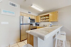 A modern kitchen with a central island, wooden cabinets, a built-in microwave, and a stainless steel refrigerator. - 2nd Floor Gulf Front Condo, Complimentary Beach Equipment, Nearby Shops & Dining (Destin)