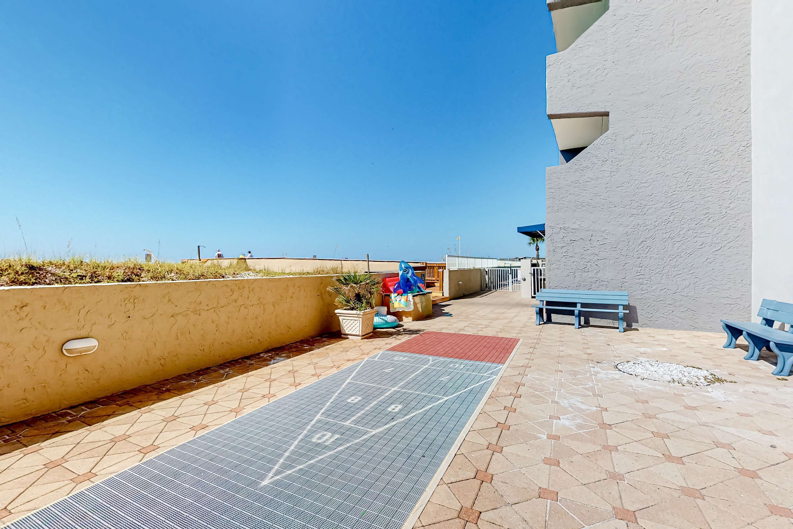 Un espace extérieur ensoleillé comprenant un terrain de jeu de «shuffleboard», des bancs et un mur.