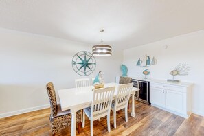 A dining area with a white table and chairs, a wooden floor, and nautical-themed wall decor. - First-floor condo with pool, ocean view, & central AC (Fort Walton Beach)