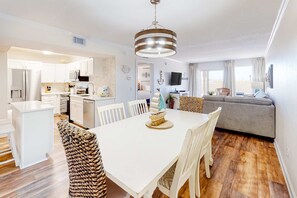 A modern kitchen with white cabinets, a dining area with a white table and chairs, and a grey sofa in the living room. - First-floor condo with pool, ocean view, & central AC (Fort Walton Beach)