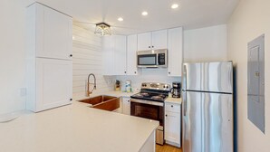 A modern kitchen with white cabinetry, stainless steel appliances, and a central island. - Modern beach condo with pool, hot tub, well-equipped kitchen, balcony, & W&D (Perdido Key)