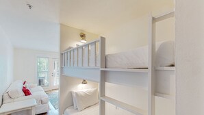 A bunk bed room with a white color scheme, a white sofa, and a small table. - Modern beach condo with pool, hot tub, well-equipped kitchen, balcony, & W&D (Perdido Key)
