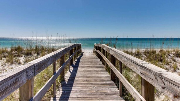 A wooden boardwalk leading to a beach with clear blue water and sandy dunes. - Modern beach condo with pool, hot tub, well-equipped kitchen, balcony, & W&D (Perdido Key)