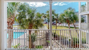 A balcony with a view of a swimming pool, palm trees, and a parking area. - Modern beach condo with pool, hot tub, well-equipped kitchen, balcony, & W&D (Perdido Key)