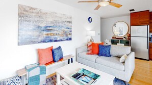 A modern living room with a grey sofa, colorful cushions, a white coffee table, and a ceiling fan. - Ground-floor condo half block from the beach with patio, central AC, pool & WiFi (Destin)