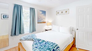 A bedroom with a bed, a ceiling fan, a window with curtains, a bedside table with a lamp, and a door. - Ground-floor condo half block from the beach with patio, central AC, pool & WiFi (Destin)
