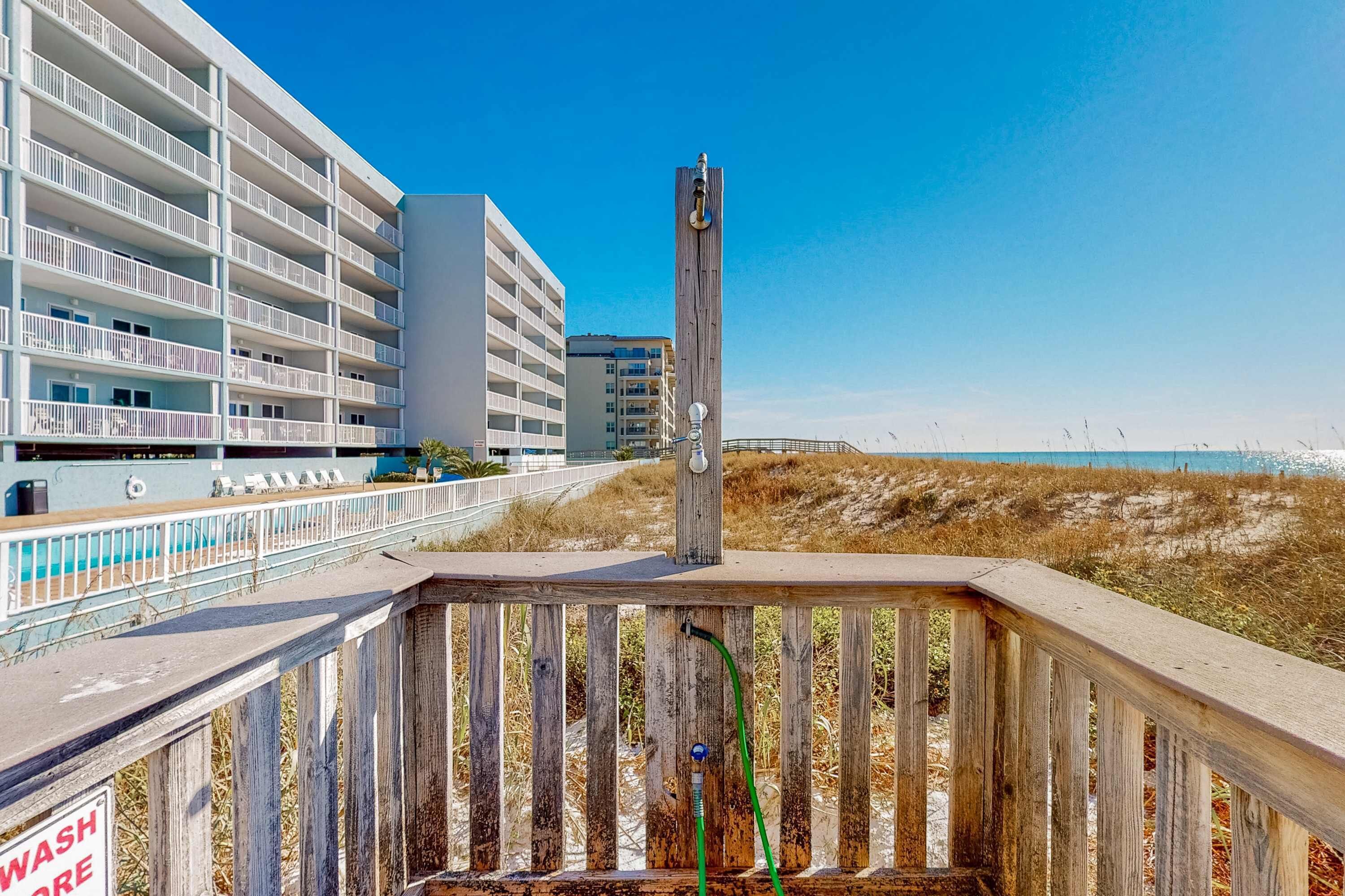 A wooden deck with a 'WASH HERE' sign, overlooking a beach with buildings in the background.