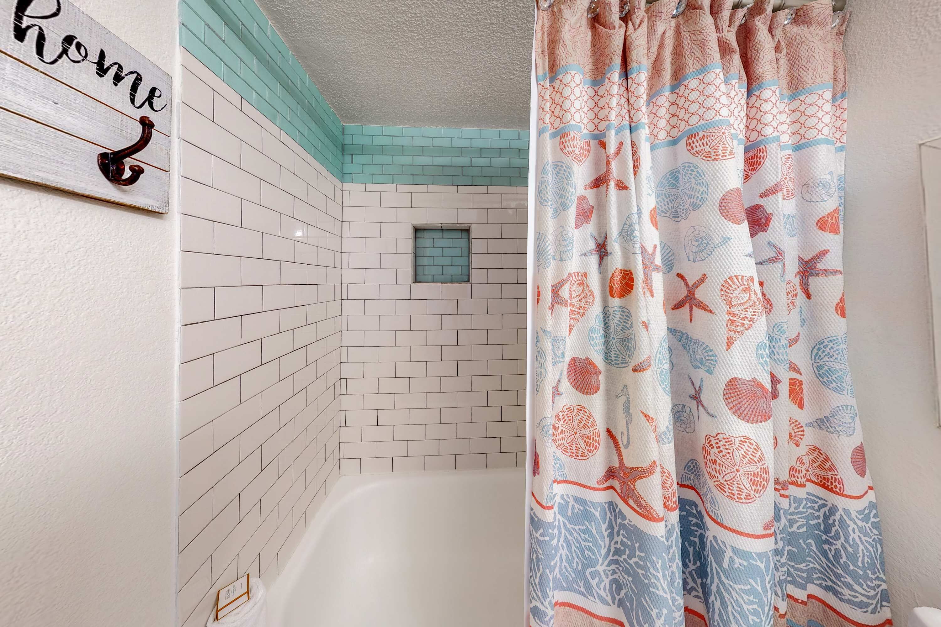 A bathroom with white tiled walls, a small window, and a shower curtain with a sea shell pattern.