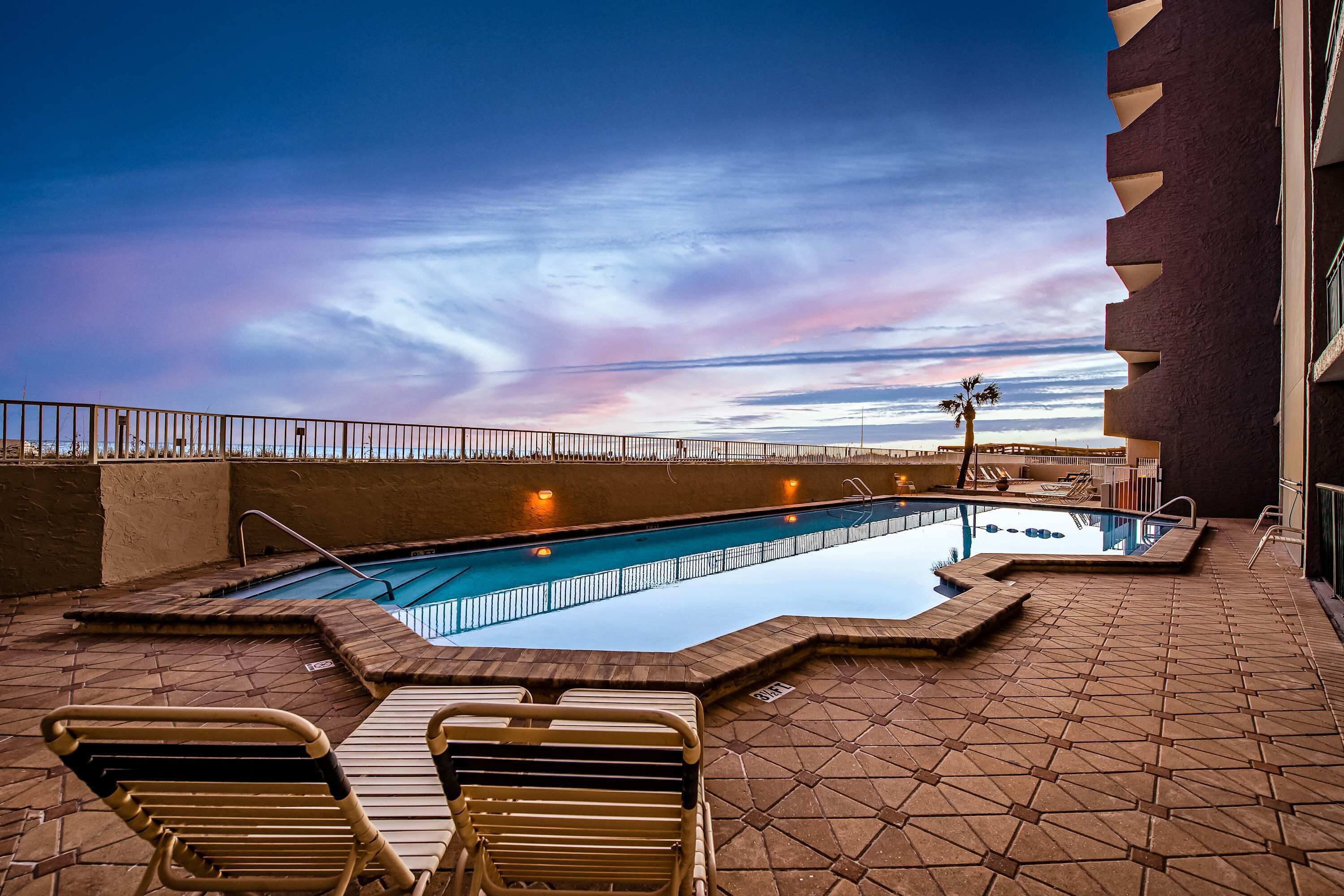 Ein Pool im Freien mit Liegestühlen, einer Palme und Blick auf den Sonnenuntergang.